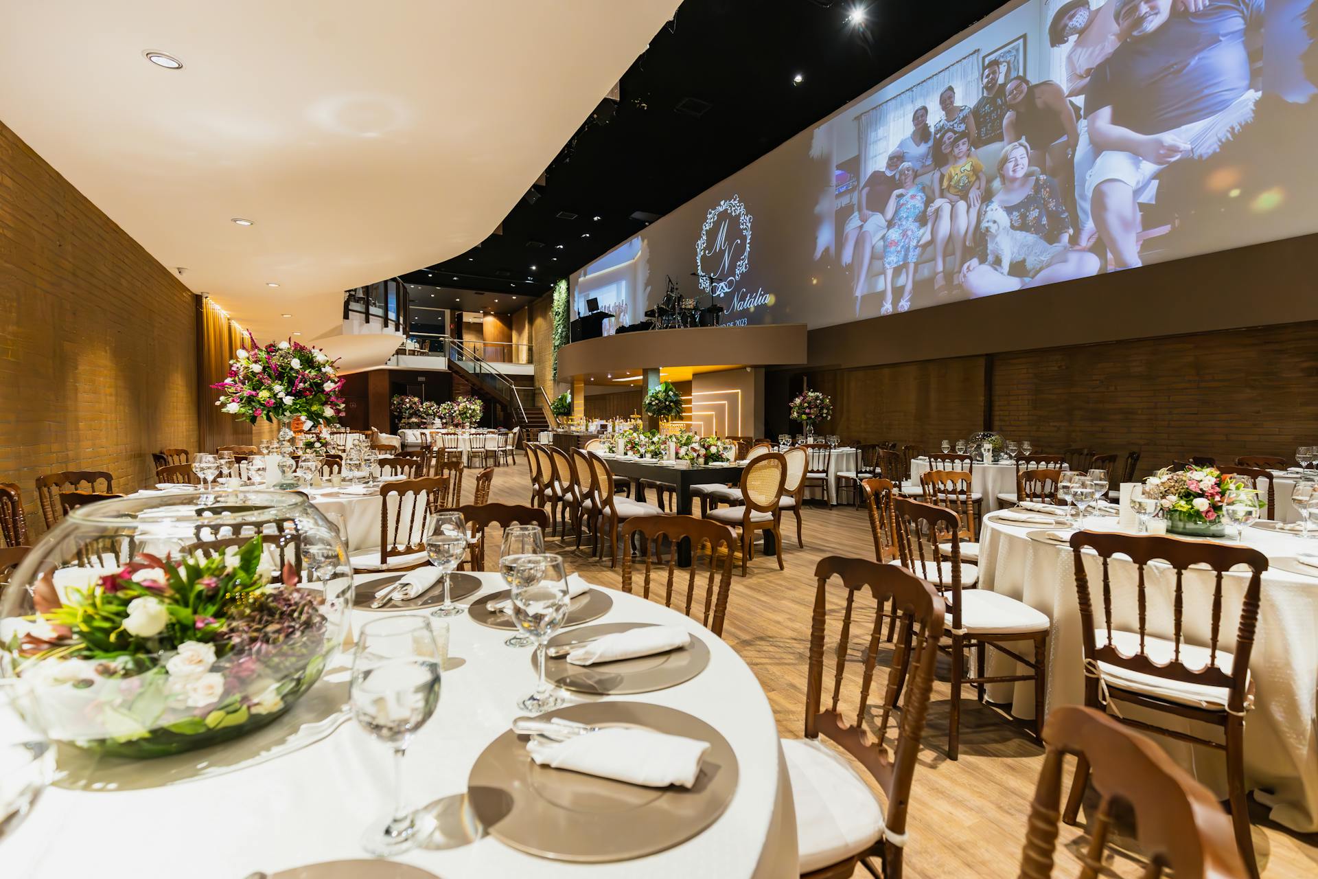 A modern function venue with tables, chairs, and a video screen for presentations or entertainment.