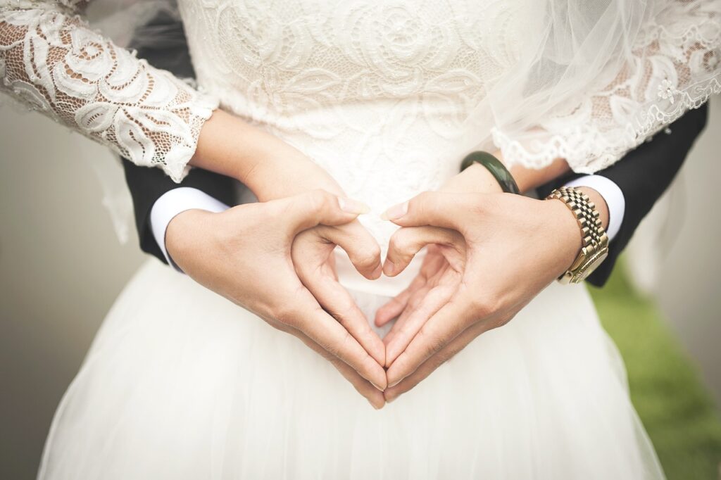 A romantic close-up of a bride and groom forming a heart shape with their hands, symbolizing love and unity at a beautiful wedding venue.