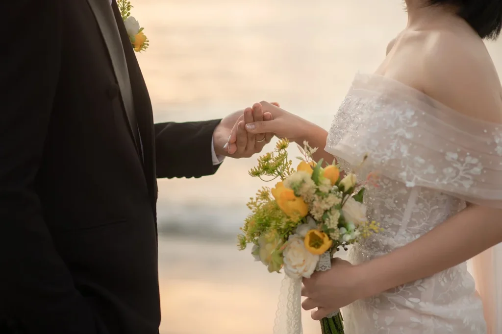 A close-up of a bride holding a bouquet while gently holding hands with the groom at a stunning wedding venue.